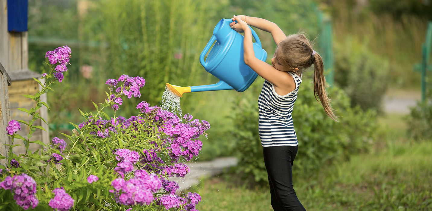 Little girl watering plants with a watering can.