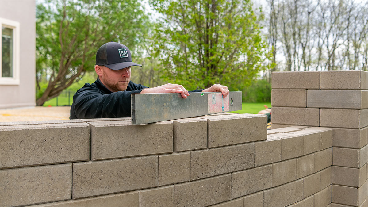 LawnCare by Walter employee maintaining our standards of quality assurance as he levels stone wall blocks during a custom retaining wall installation.