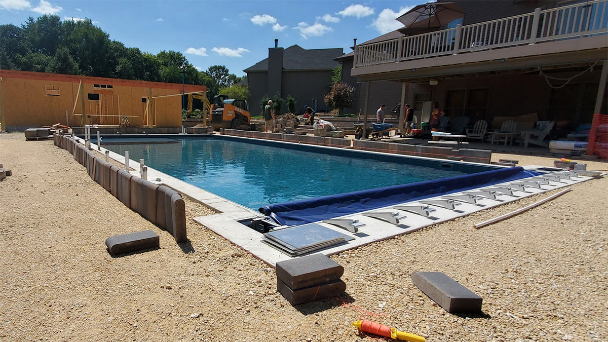 Hardscape and pavilion framing for a custom paver patio surrounding an in-ground swimming pool.